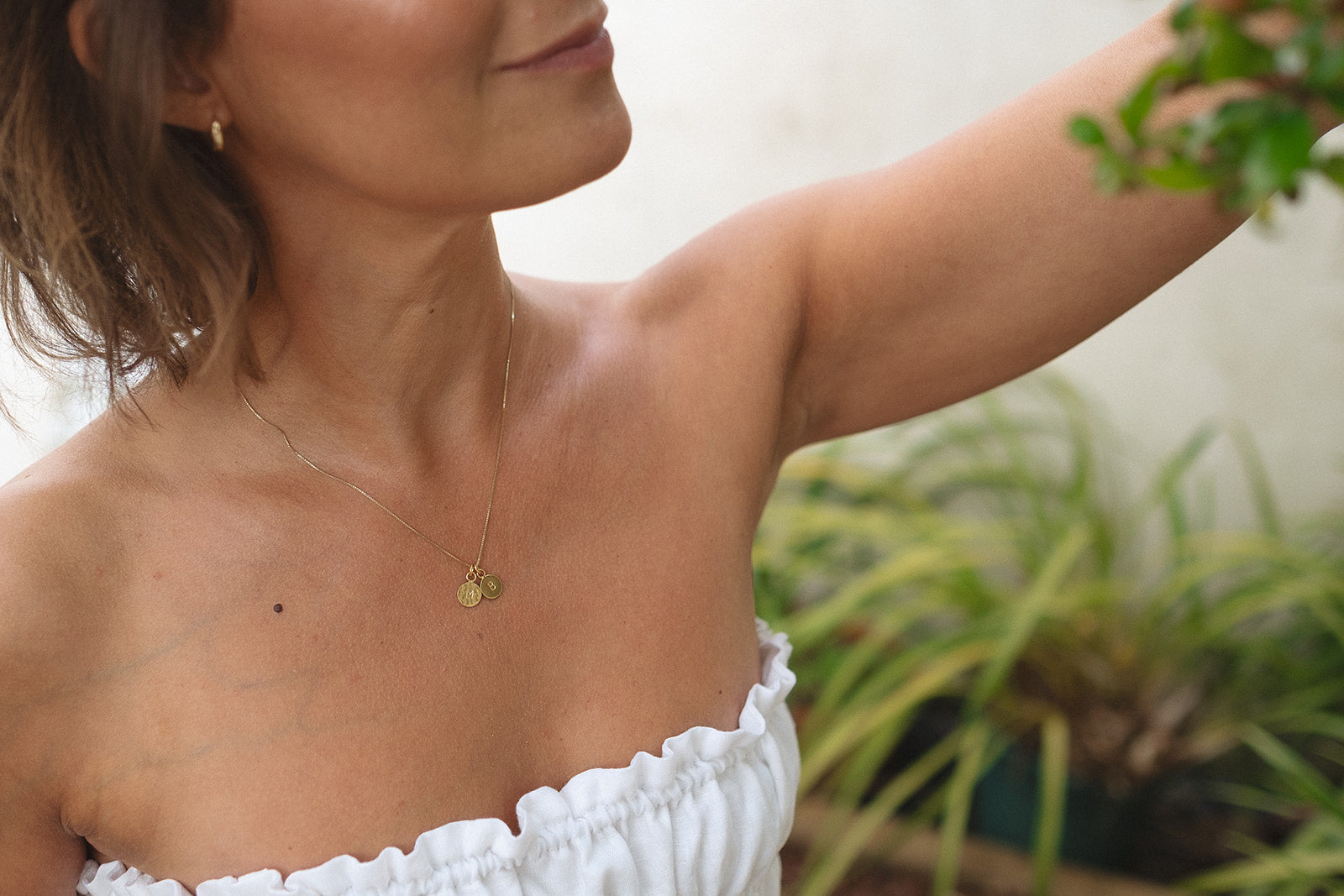 a woman wearing a gold necklace with two initials on it